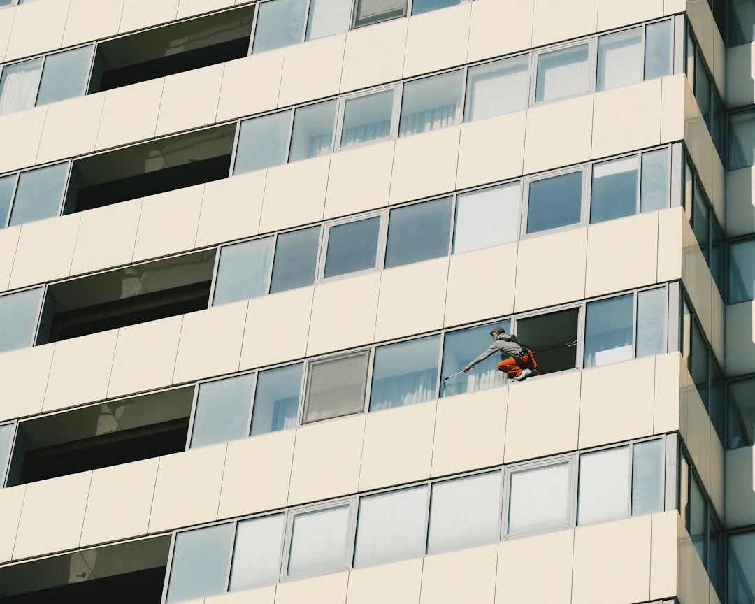 services-02 Three window cleaners suspended on ropes clean a modern glass building facade during the day.